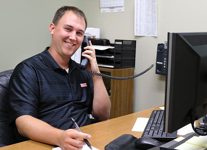 Man talking on the phone while taking notes and smiling at the camera