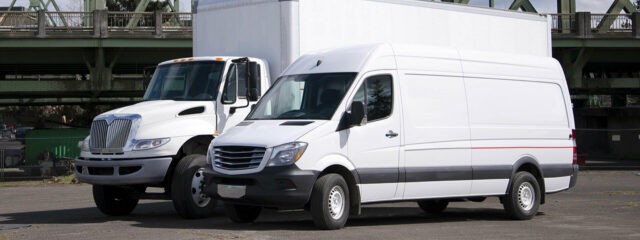 A white box truck behind a white cargo van
