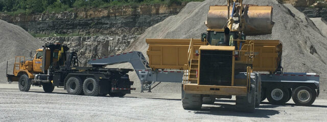 Work trucks in a quarry, one with a dump trailer.